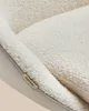 Close-up view of a cream-colored, sherpa-upholstered chair with a small tan tag sewn into the seam. Náhled obrázku produktu