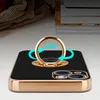A black phone case with a gold ring holder is shown on a table, with books and a textured cloth in the background. Produktbild-Vorschau