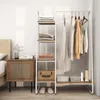 A white metal and wood garment rack with shelves and clothes hanging on it, placed next to a bedside table and a bed. Produktbild-Vorschau
