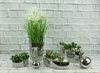 A collection of silver ceramic planters with artificial plants and decorative balls, set against a white brick wall. Podgląd zdjęcia produktu