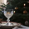 A dessert in a glass goblet is placed on a plate in front of a decorated Christmas tree. Náhled obrázku produktu