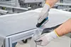 A person wearing protective gloves is using a cutter to cut a sheet of plastic material on a table in a factory setting. Voir les images du produit