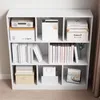 A white, multi-compartment bookshelf filled with books, boxes, and decorative items, set against a neutral background. Produktbild-Vorschau