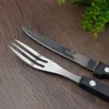 A close-up shot of a steak knife and fork set on a wooden surface. Voir les images du produit