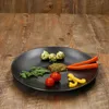 A black plate with food items on a wooden table. Produktbild-Vorschau