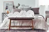 A bedroom scene with rolled-up duvets displayed on a bench in front of a bed. Produktbild-Vorschau