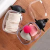 Two clear containers with black sheep-shaped lids, one filled with cotton pads and the other with makeup sponges, sit on a wooden surface. Náhľad obrázku produktu