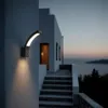 An outdoor wall lamp illuminates a pathway and stairs leading to a building by the sea at dusk. Anteprima dell’immagine prodotto