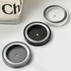 Three circular bathroom accessory holders are arranged on a white surface, with a partial view of a branded item in the background. Produktbild-Vorschau