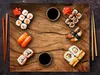 A top-down view of a wooden table with various sushi dishes, soy sauce, and chopsticks. Produktbild-Vorschau