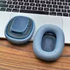 Two blue ear pads for headphones are placed on a wooden surface next to a laptop keyboard. Produktbild-Vorschau