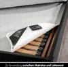 A close-up view of a mattress protector being placed on a slatted bed base. Produktbild-Vorschau