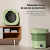 A collapsible washing machine is shown in two states: open and folded, next to a wooden shelf with folded towels. Náhled obrázku produktu