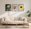 A living room scene with a sofa, coffee table, and framed pictures of flowers on the wall. Produktbild-Vorschau