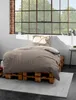 A bed with brown bedding is set up on wooden pallets in front of a large window. Produktbild-Vorschau