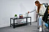 A woman is reaching for glasses on a shelf next to a small plant and a framed picture. Produktbild-Vorschau