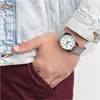 A person wearing a denim jacket and burgundy pants has their hand in their pocket, showing a silver watch on their wrist. Produktbild-Vorschau