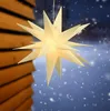 A lit star decoration hangs outdoors in the snow, with a wooden structure to the left. Náhled obrázku produktu