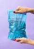 Hands holding a blue bag of almonds in dark chocolate. Produktbild-Vorschau