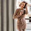 A woman stands on a balcony, holding a mug and touching her hair, with a curtain and a building in the background. Podgląd zdjęcia produktu