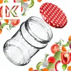 A clear glass jar with a red lid patterned with white hearts, surrounded by fresh vegetables and herbs. Produktbild-Vorschau