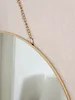 A close-up of a round mirror with a gold metal frame, hanging from a gold chain against a textured pink and white wall. Produktbild-Vorschau