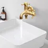 A brass wall-mounted faucet with two outlets is shown above a white sink, with water flowing from one of the outlets. Podgląd zdjęcia produktu