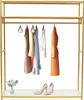 A gold metal clothing rack with several garments hanging on it, and a pair of high heels and a small vase of flowers on the bottom shelf. Podgląd zdjęcia produktu