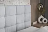 A close-up view of a bed's upholstered headboard and a bedside table with decorative items. Produktbild-Vorschau