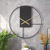 A modern black and gold wall clock is displayed on a gray concrete wall, with a potted plant and a vase of flowers in the foreground. Produktbild-Vorschau