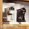 Two coffee machines, one new and one old, are displayed side-by-side on a shelf, highlighting the difference in mug space. The new model is beige, and the old model is black. Text overlays indicate the 'NEW' and 'Old' models and provide measurements for mu Produktbild-Vorschau