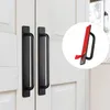 Two black cabinet handles are shown attached to white cabinet doors. A circular inset shows a close-up of one handle with its adhesive backing being peeled off. Produktbild-Vorschau