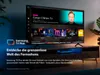 A Samsung TV displaying the Samsung TV Plus interface, set on a TV stand in a living room. Produktbild-Vorschau