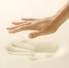 A hand gently pressing into a soft, cream-colored material, leaving an indentation. Produktbild-Vorschau