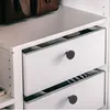 Close-up of white drawers with black knobs in a closet, with brown bags on the shelf above. Produktbild-Vorschau