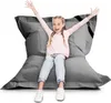 A young girl is sitting on a large grey beanbag chair with her arms raised in excitement.