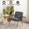 A gray armchair is placed next to a small side table with a vase of plants and a cup on it. The scene is set in a room with a patterned rug and blinds in the background. Produktbild-Vorschau