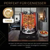 A döner grill with meat skewers cooking, set on a wooden table with a plate of vegetables and a living room in the background. Náhled obrázku produktu