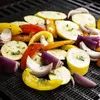 Nahaufnahme einer schwarzen Grillmatte aus Netz, bedeckt mit bunten geschnittenen Gemüsesorten wie Zucchini, Paprika und roten Zwiebeln Productafbeelding-voorbeeld