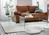 A living room scene with a brown sofa, glass coffee tables, and a rug. Podgląd zdjęcia produktu