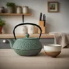 A green cast iron teapot and a ceramic cup are placed on a wooden table in a kitchen setting. Podgląd zdjęcia produktu