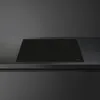 A black induction hob is shown on a dark countertop. Voir les images du produit