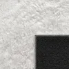 A close-up view of a white shaggy rug, showing the texture of the material and the black backing with white dots. Produktbild-Vorschau