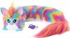 A rainbow-colored Furby toy with a long body and tail, lying on a white background. A small purple comb is placed next to it. Produktbild-Vorschau