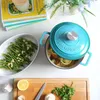A top-down view of a teal Dutch oven filled with food, next to a dish of green beans and a cutting board with ingredients. Produktbild-Vorschau