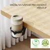 A coffee cup holder attached to the edge of a wooden desk, with white curtains in the background. There are two certification badges at the bottom right. Náhled obrázku produktu
