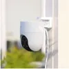 A white security camera mounted on a white pole outdoors, with green foliage in the background. Anteprima dell’immagine prodotto