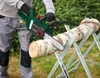 A person is using a cordless chainsaw to cut a log that is supported by a sawhorse. Produktbild-Vorschau