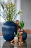 A collection of decorative items including wooden monkey figures, vases with flowers, and potted plants on a table. Anteprima dell’immagine prodotto