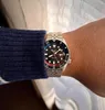 A person wearing a watch on their wrist, with a blue sweater sleeve visible. Produktbild-Vorschau